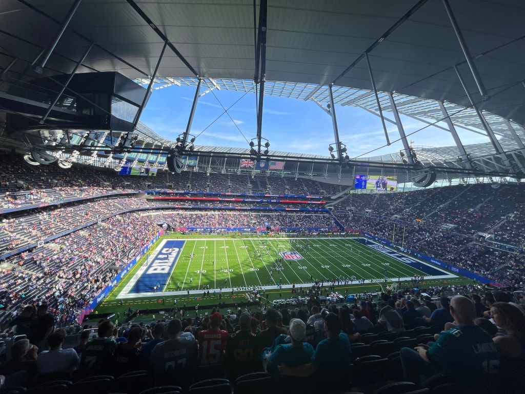 A wide view from section 507, row 21, seat 236 at Tottenham Hotspur Stadium. The stadium is half full, pre-kick-off and the sky is  blue.