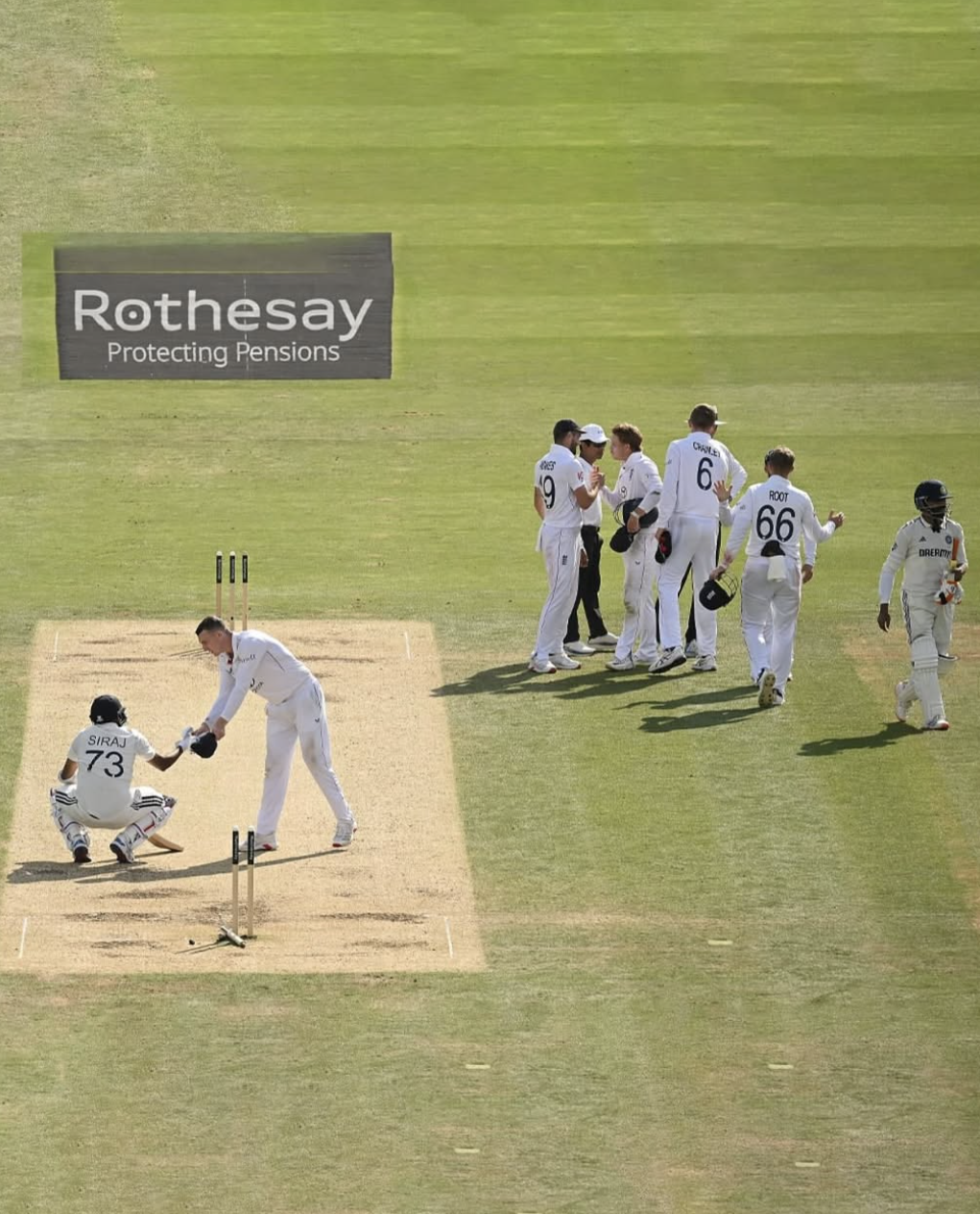 Harry Brook shakes Mohammed Siraj's hand. Siraj is squatting with his batting equipment on. The England team celebrate to the right -hand side of the image.