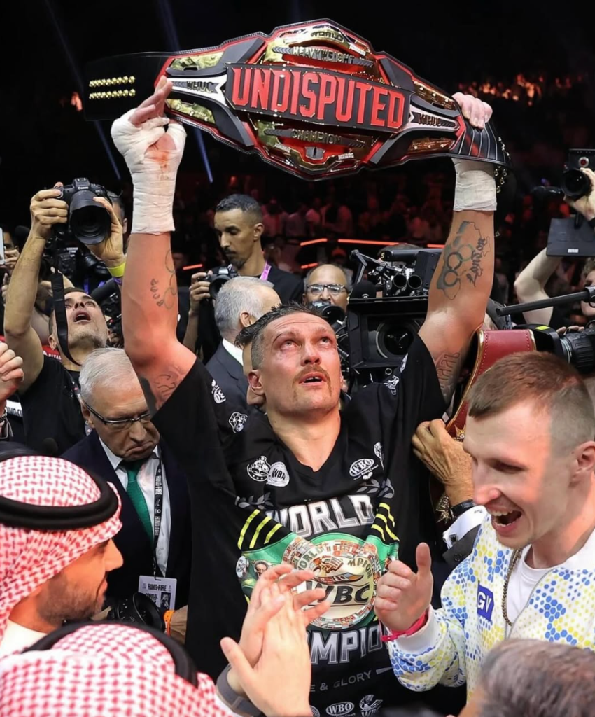 This photo shows Oleksandr Usyk lifting the undisputed belt above his head, whilst he looks to the sky after his victory against Tyson Fury.