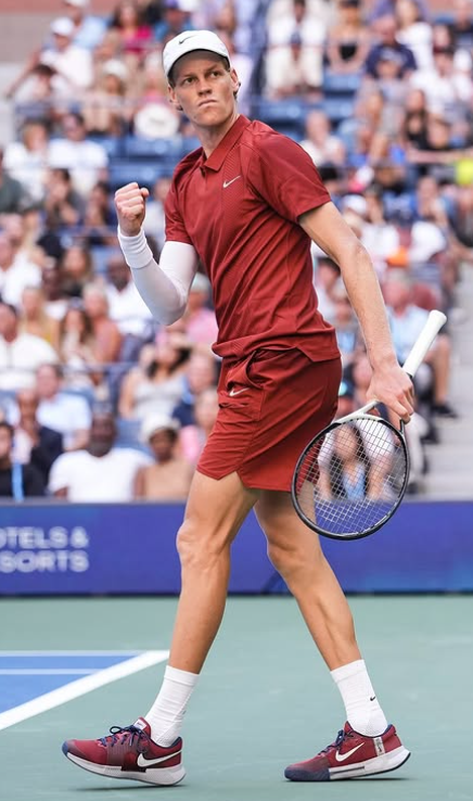 This photo shows Jannik Sinner with a stern look on his face. His right fist is closed, and he is holding his tennis racket in his left hand.